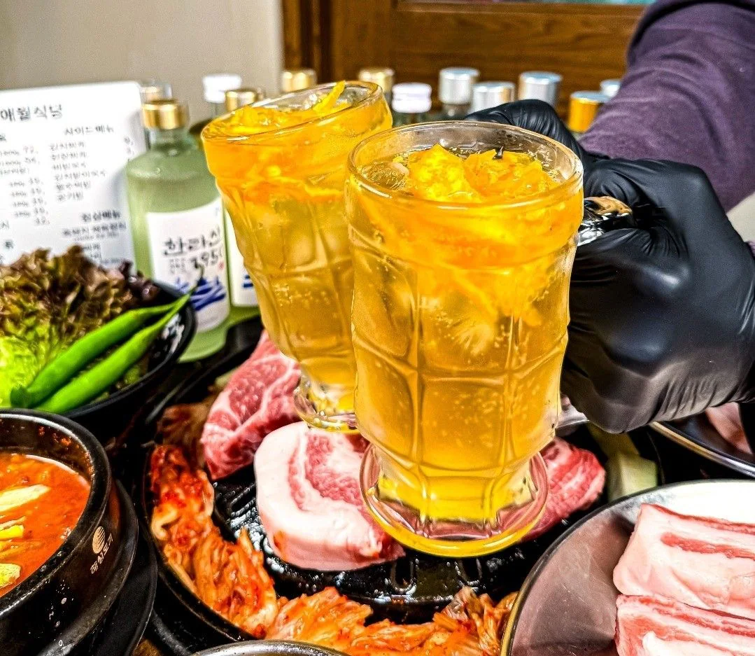 在餐桌上方乾杯的兩杯橘色濟州柚子高球