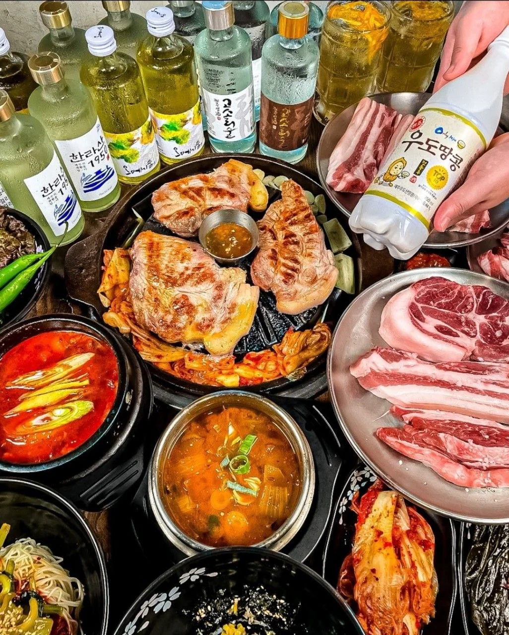 涯月食堂 狎鷗亭店的餐桌:烤盤上的豬肉、生肉盤、湯鍋與濟州酒瓶